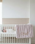 Nursery room with a white crib, pink blanket, and wooden rocking chair.