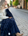 Woman sitting outdoors with a blue blanket, holding a gold cup.
