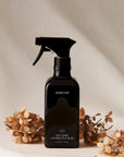 Black spray bottle labeled 'HOMEcourt' with dried flowers on a neutral background