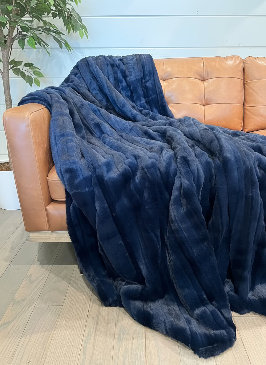 Blue blanket draped over a brown leather sofa against a light blue wall.