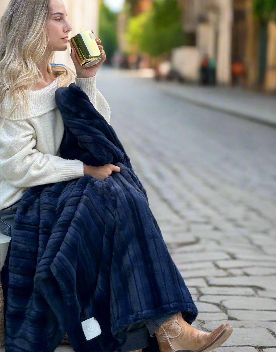 Woman sitting outdoors with a blue blanket, holding a gold cup.