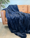 Blue blanket draped over a brown leather sofa against a light blue wall.